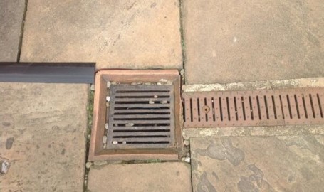 Speaker cables run through gaps in the paving and into a drainage channel
